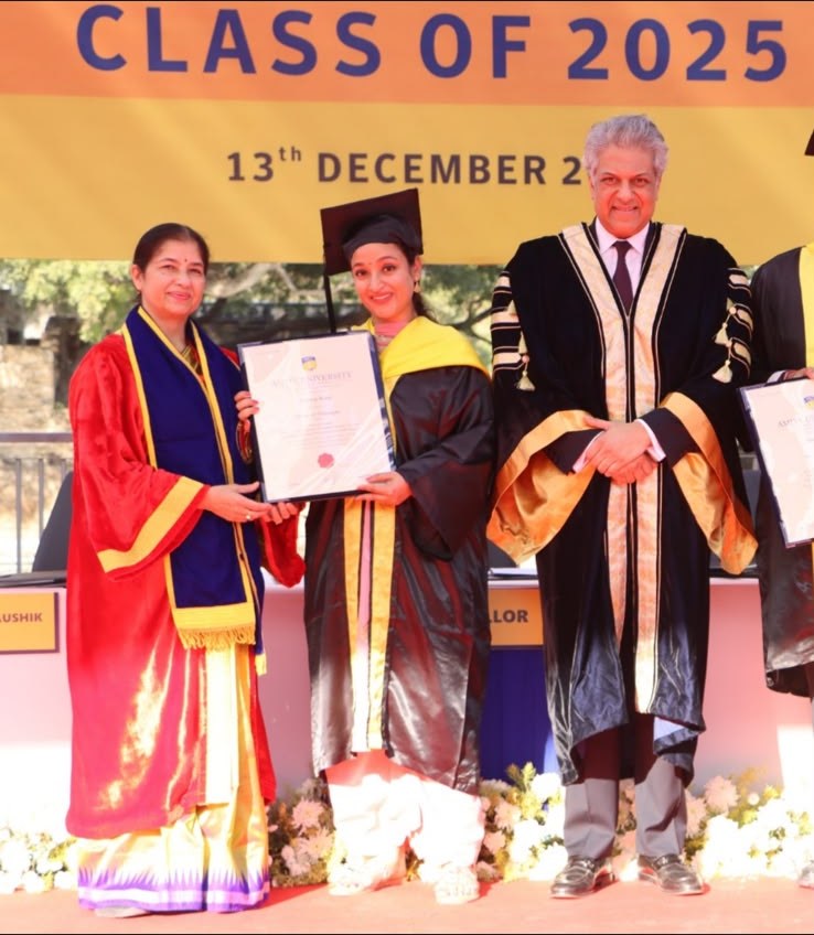Dr. Jasdeep Kaur in academic gown and hood on a convocation stage, holding her certificate, flanked by two university officials, beneath a banner reading Class of 2025.
